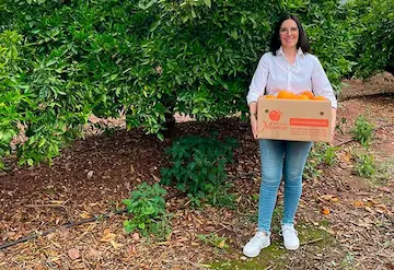 Marisa la propietaria en su huerto sosteniendo una caja de Naranjas